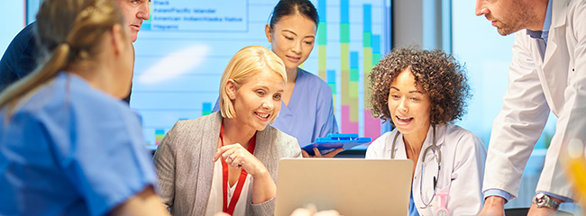 Healthcare professionals and analysts engaging in collaborative adult learning on a laptop.